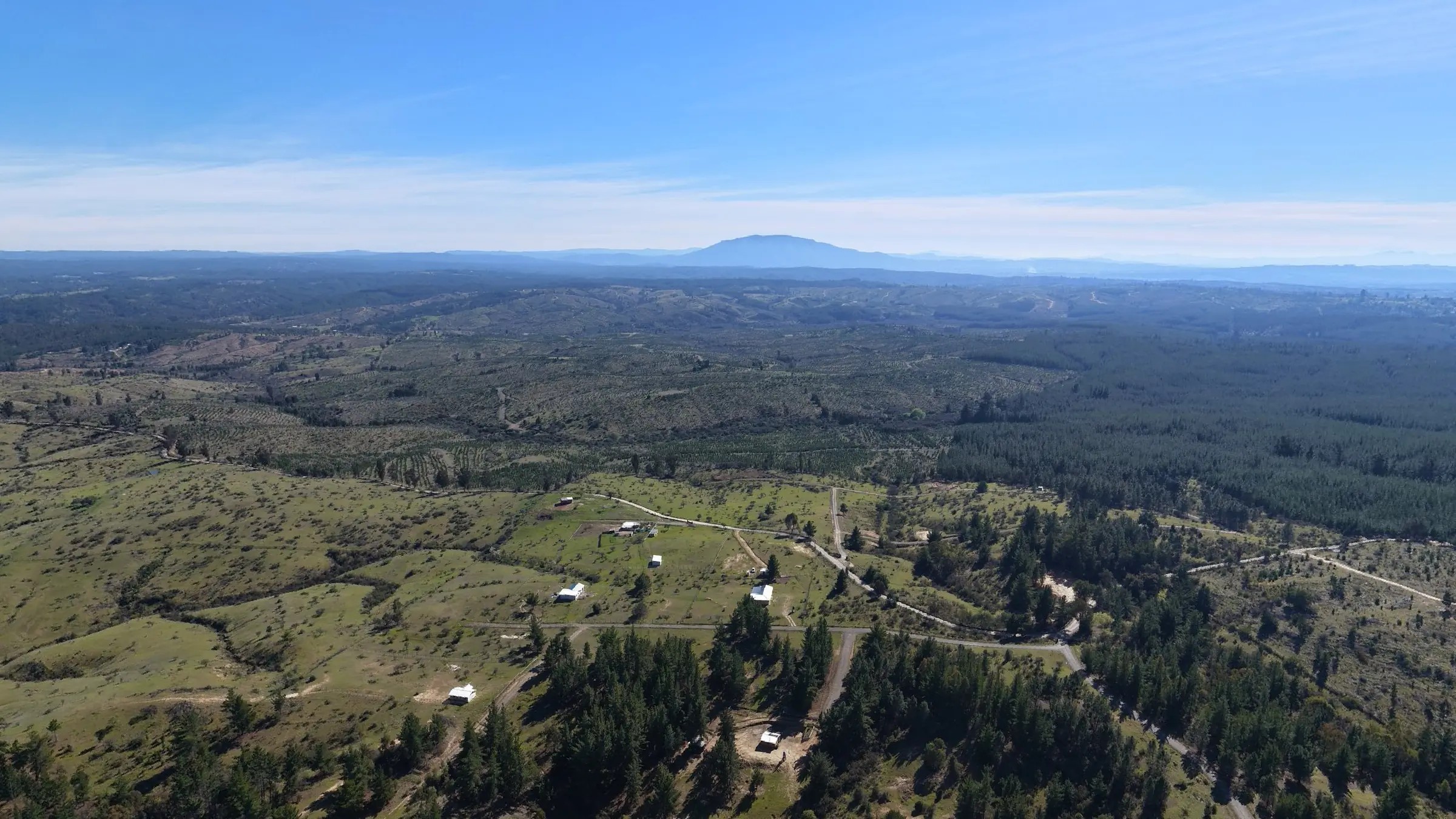 Vista aérea de un loteo en Cauquenes: parcelas, caminos de tierra y el volcán en el horizonte.